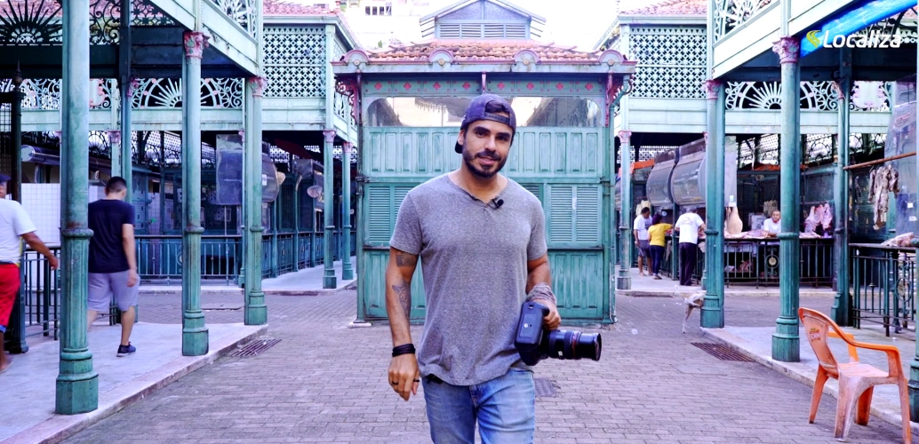 Fotógrafo Ricardo Martins caminha por feira segurando câmera em dia claro