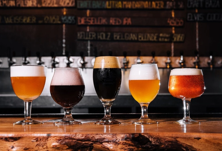 Vários copos de cerveja artesanal de diferentes cores sob um balcão de um bar