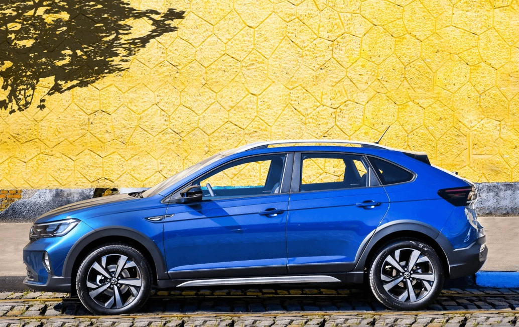 Volkswagen Nivus azul estacionado em uma rua de pedras em frente a um muro amarelo.