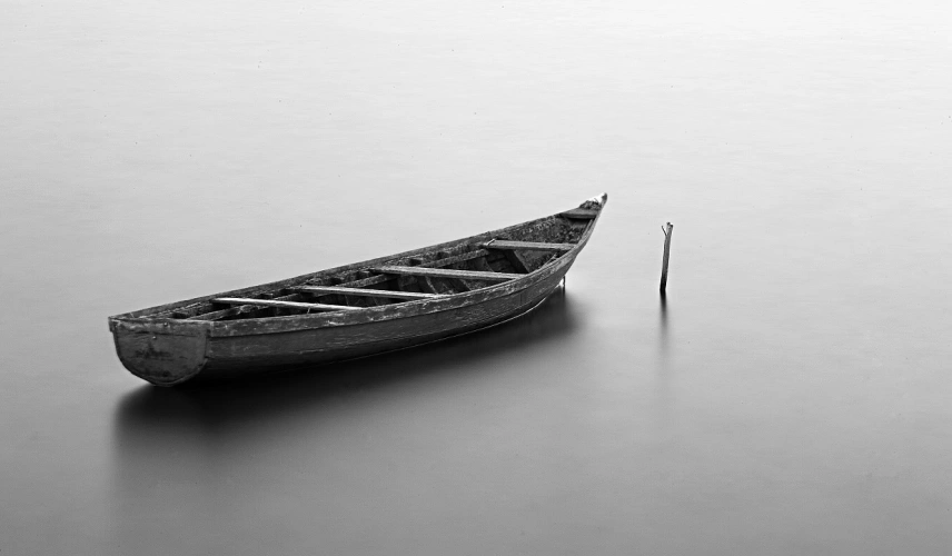 Foto em preto e branco. Em destaque, uma canoa típica brasileira sobre calmo e estático rio.