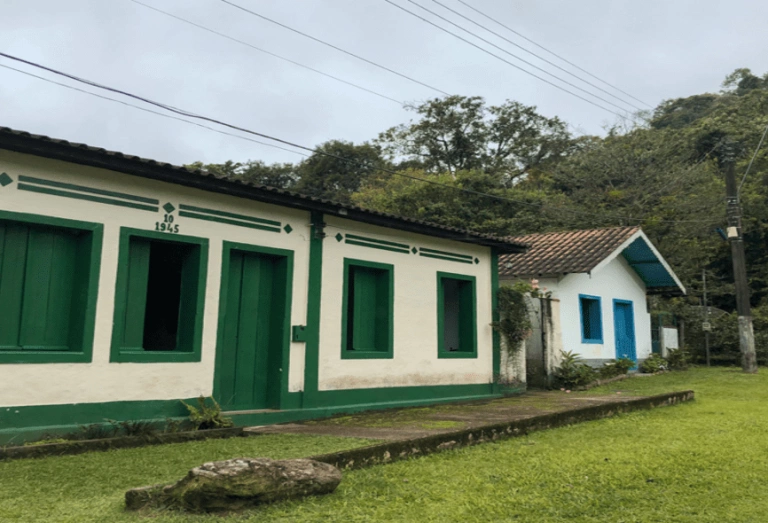 Vista semi frontal de duas casas antigas coloridas ao lado de uma densa mata no município de Visconde de Mauá