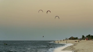 Praia com alguns turistas na areia, enquanto outros praticam kitesurf
