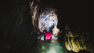 Homem de capacete com lanterna sentado próximo a um poço às estruturas de uma caverna escura