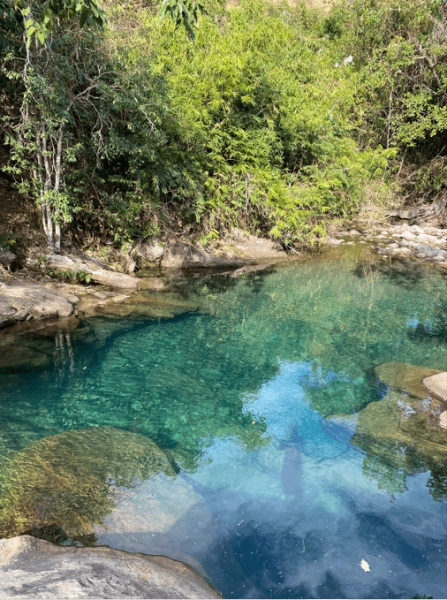Poço de água azul cristalina cercado por pedras e vegetação