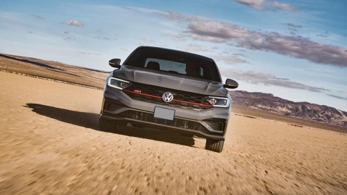 Frente de um Volkswagen Jetta 2020 em movimento em um deserto com montanhas ao fundo.