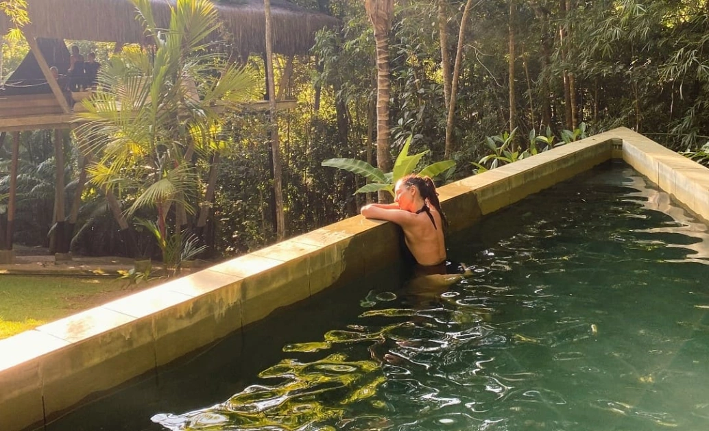 Mulher se banha em piscina instalada em região florestal em dia claro