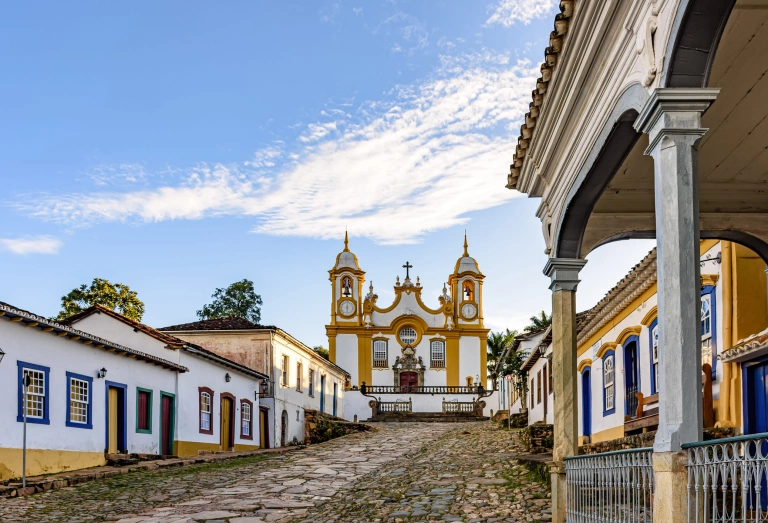Uma rua histórica tranquila na cidade de Tiradentes, em Minas Gerais, com casas coloniais e uma igreja barroca ao fundo