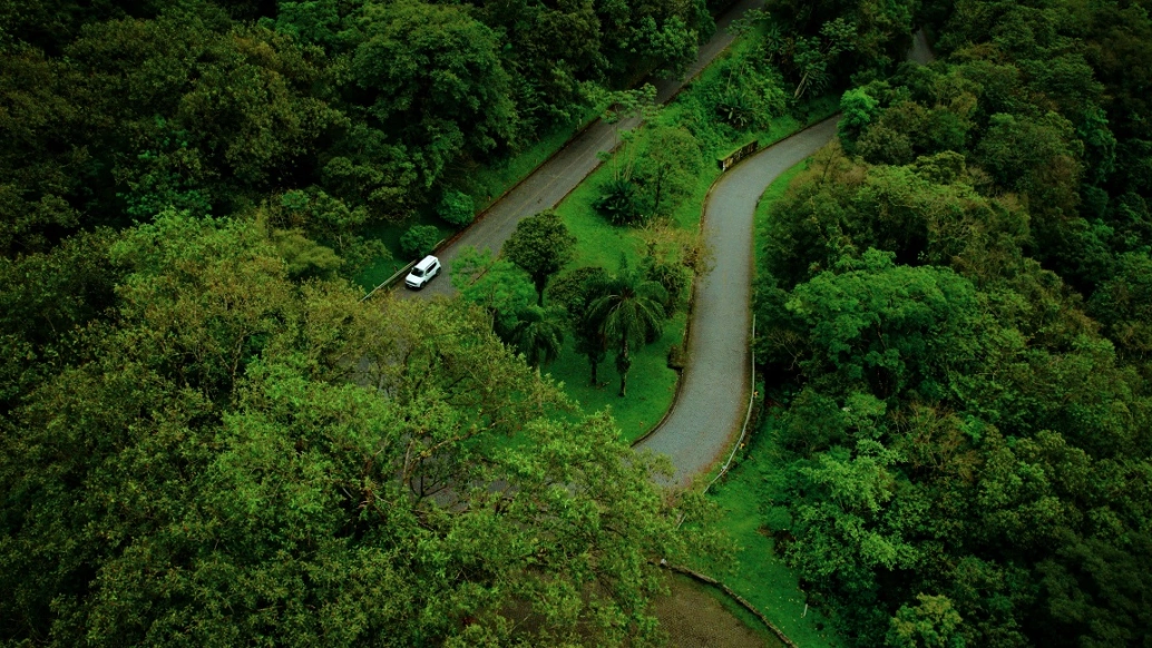 Vista aérea da estrada Graciosa, rumo à Serra da Graciosa. Vemos uma paisagem vibrante, esverdeada e diversa, além de duas pistas, uma curva e outra reta.