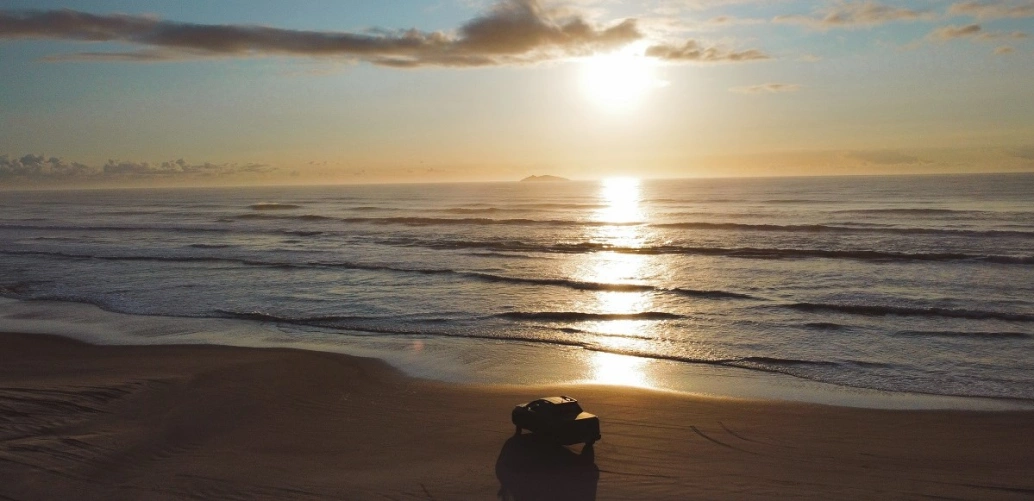 Paisagem de nascer do sol com carro estacionando na areia de praia deserta