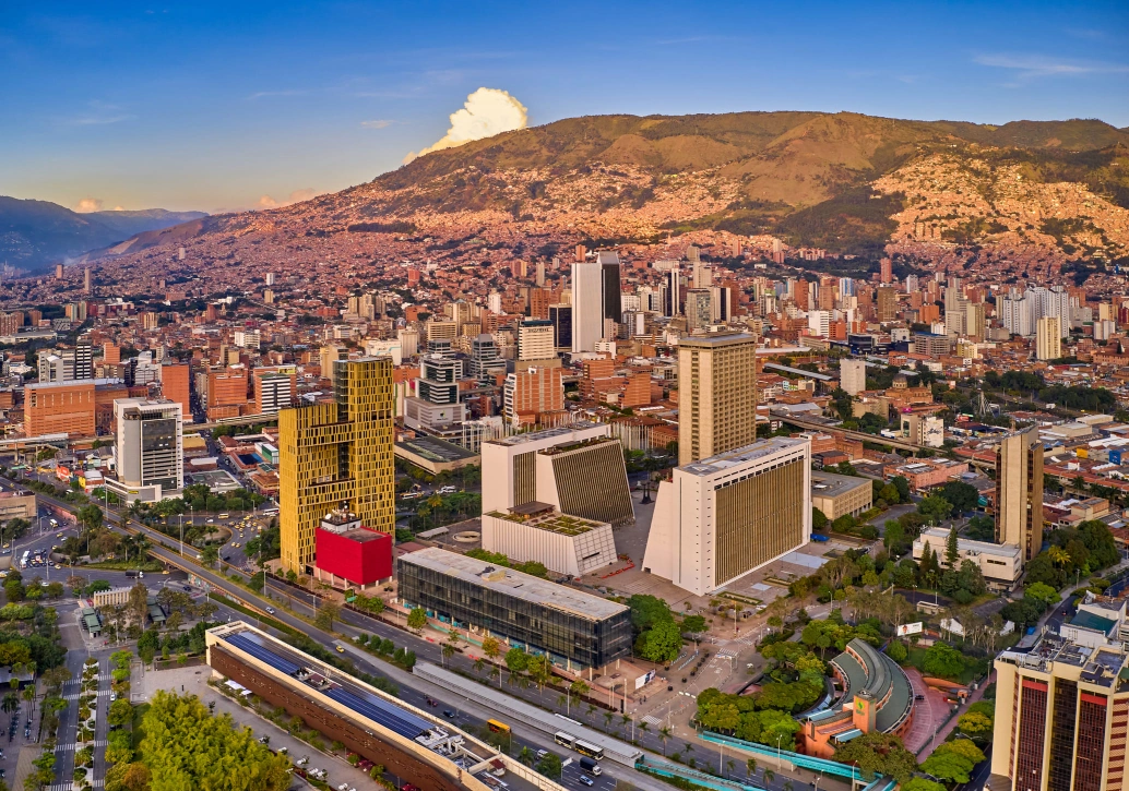 Vista aérea da cidade de Medellín, com alguns edifícios modernos em destaque e uma enorme montanha com cobertura vegetal ao fundo
