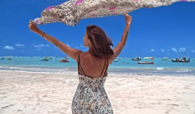 Mulher de costas levanta lenço em frente a praia de águas azuis em dia ensolarado