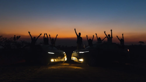 Várias pessoas com braços levantados posando com dois carros em bonita paisagem de pôr do sol