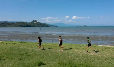 Três pessoas correndo na margem de uma praia em dia ensolarado em Paraty
