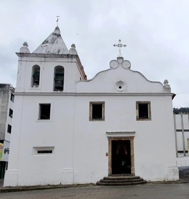 Destaque para uma igreja de arquitetura muito simples, com pintura branca e pequenas janelas