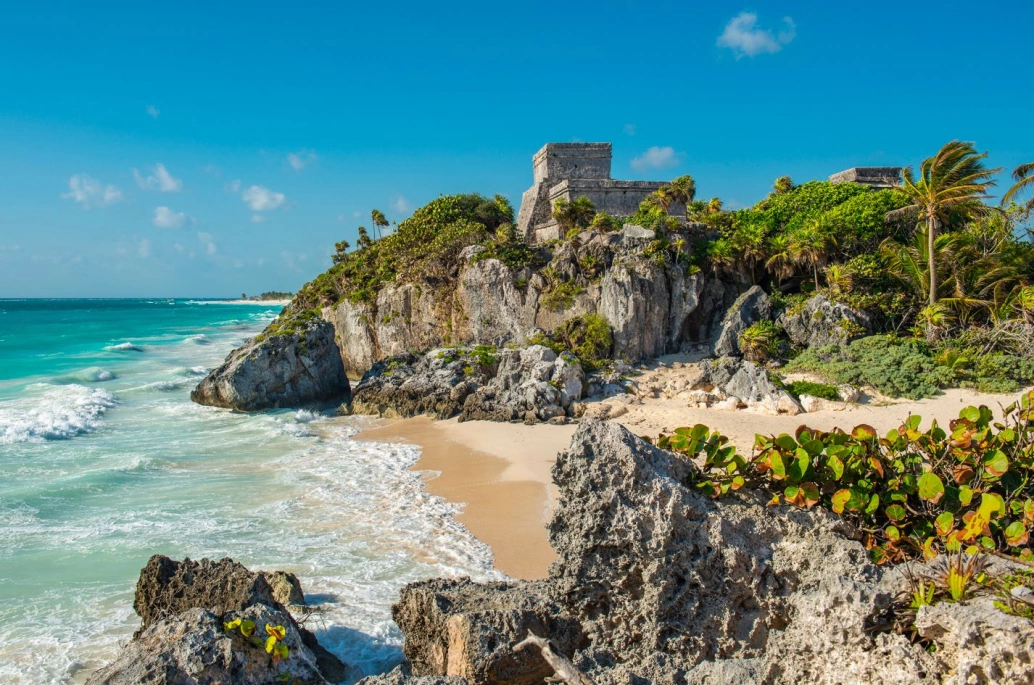 Paisagem caribenha, com céu azul, mar translúcido e ruínas de antiga civilização antiga.