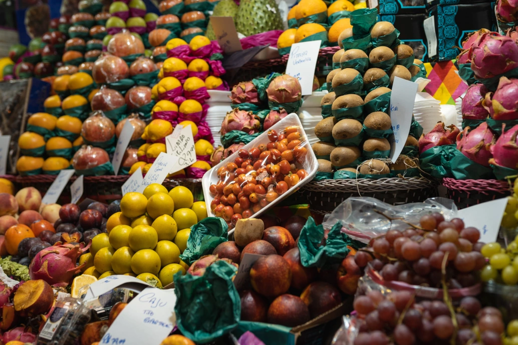 Banca com uma variedade de frutas no Mercado Municipal de SP. Há uvas, kiwis, pitayas, limões e outras frutas frescas.
