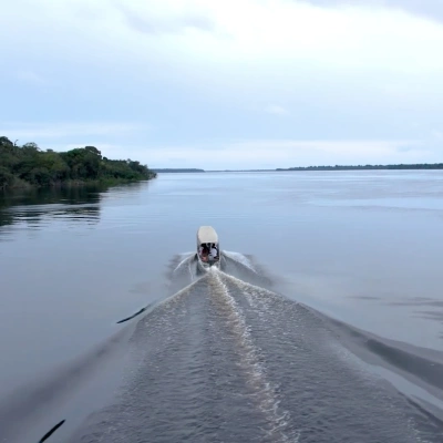 Barco navegando por vasto rio amazônico margeado por vegetação ativa