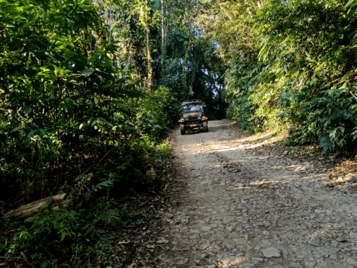 Carro Jeep passando por uma estrada de pedra em meio à vegetação densa