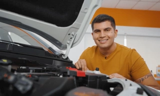 O especialista em autos e influenciador Xenão sorri ao lado do motor de um carro.