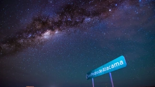 Céu extremamente estrelado, que possibilita ver as constelações e uma galáxia. Uma placa na beira da estrada indica a direção para San Pedro de Atacama