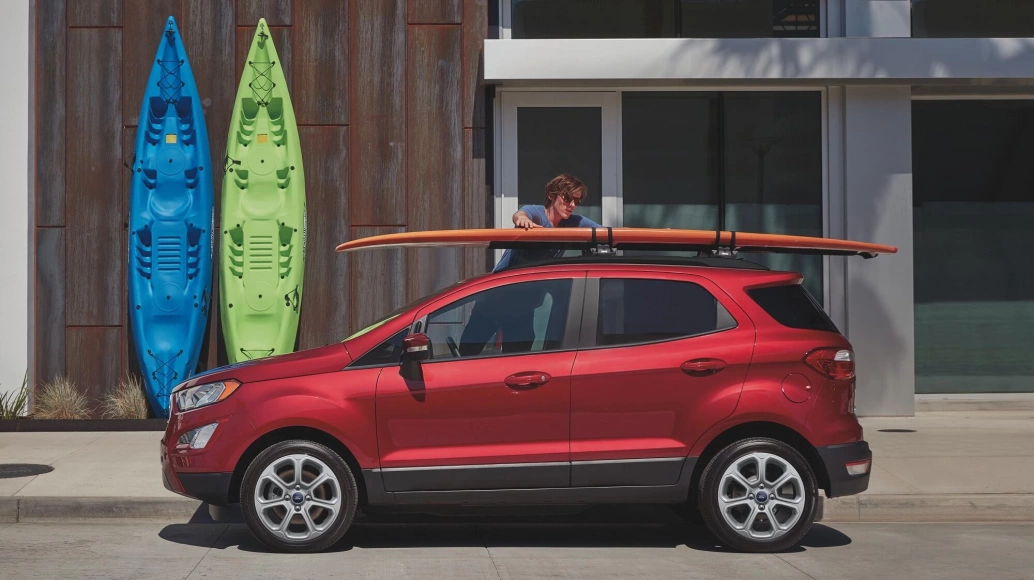 Homem coloca uma prancha de surfe em cima de um Ford EcoSport vermelho.