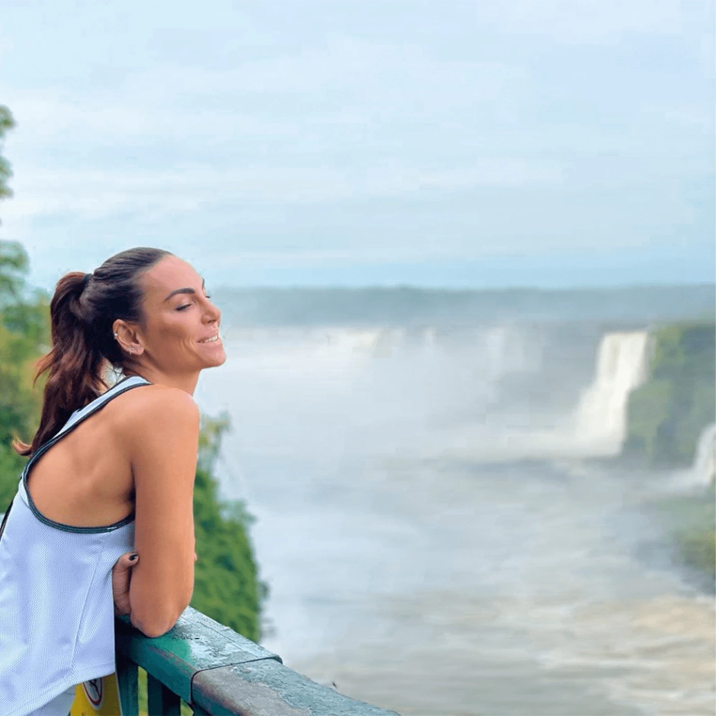 Mulher debruçada na grade sorri ao contemplar as Cataratas do Iguaçu