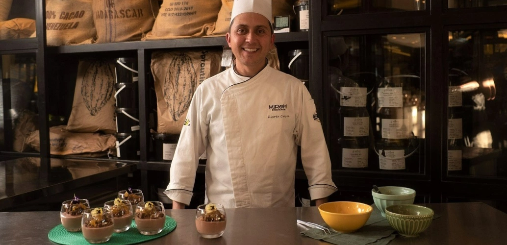 Chef Ricardo Campos sorrindo em frente a mesa contendo sobremesas