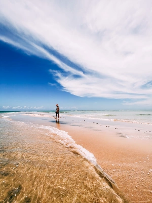 Gabriel Elias anda pelas claras areias das praias  do Morro de São Paulo (BA) com um lindo e vibrante céu azul ao fundo.