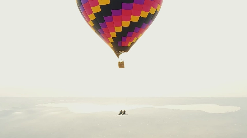 Vista panorâmica do balão voando e, pendurado nele, a mesa onde alguns aventureiros tomam café da manhã.