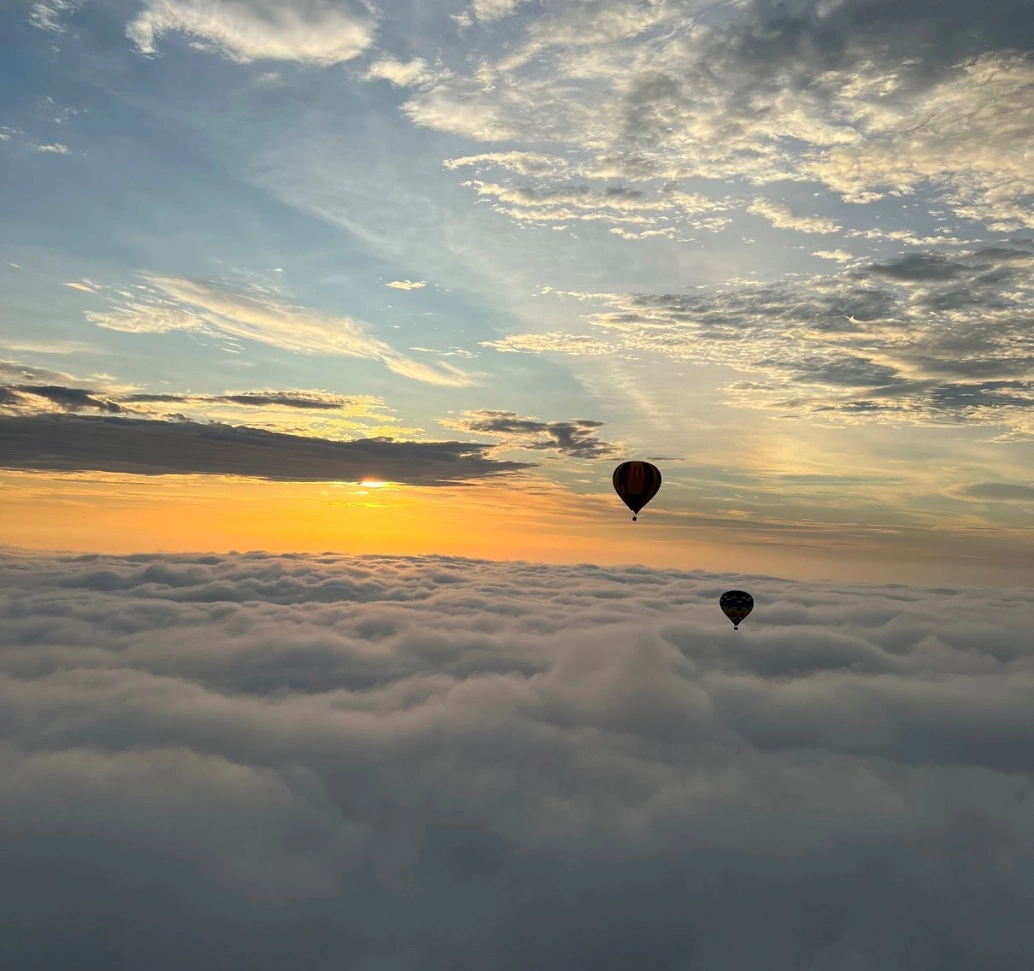 Dois balões sobrevoam nuvens em céu azul com raios de sol