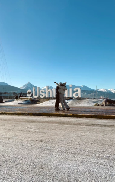Um casal posa diante do icônico letreiro de Ushuaia, em meio a uma paisagem coberta de neve.