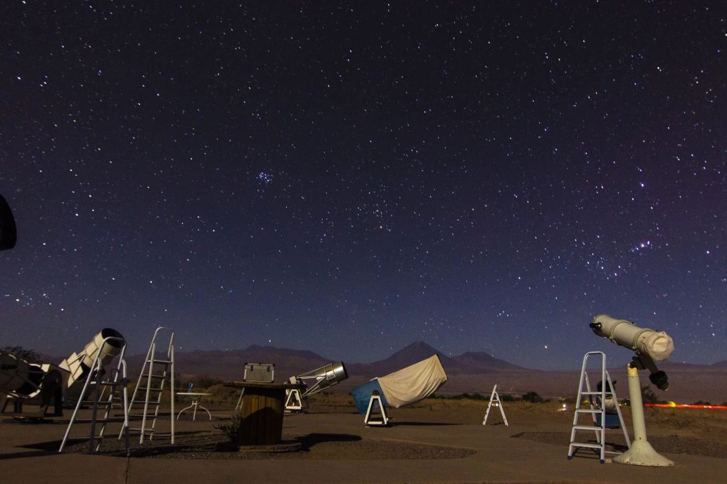 Campo aberto com céu estrelado e diversos telescópios sobre o solo