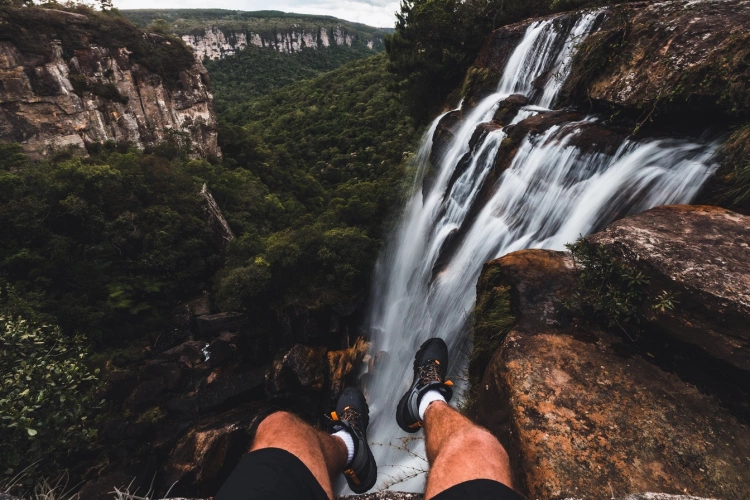 Pernas de uma pessoa sentada em pedras da Cachoeira do Butiá, localizada no Paraná.