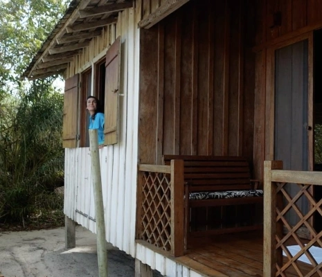 Fachada de uma casa com paredes de madeira com uma mulher olhando para fora em uma janela