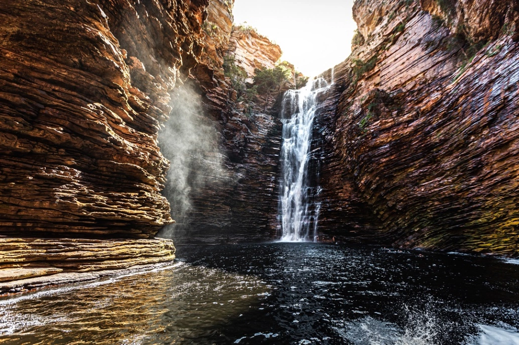 Uma cachoeira com enorme queda d'água cercada por formações rochosas até o alto.