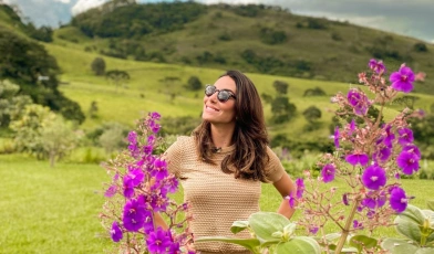 Mulher sorrindo em volta de flores de cor lilás em campo rural
