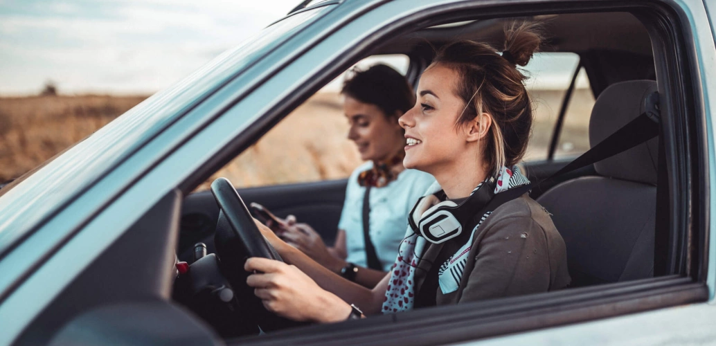 Mulher jovem dirige um carro com a amiga ao lado.