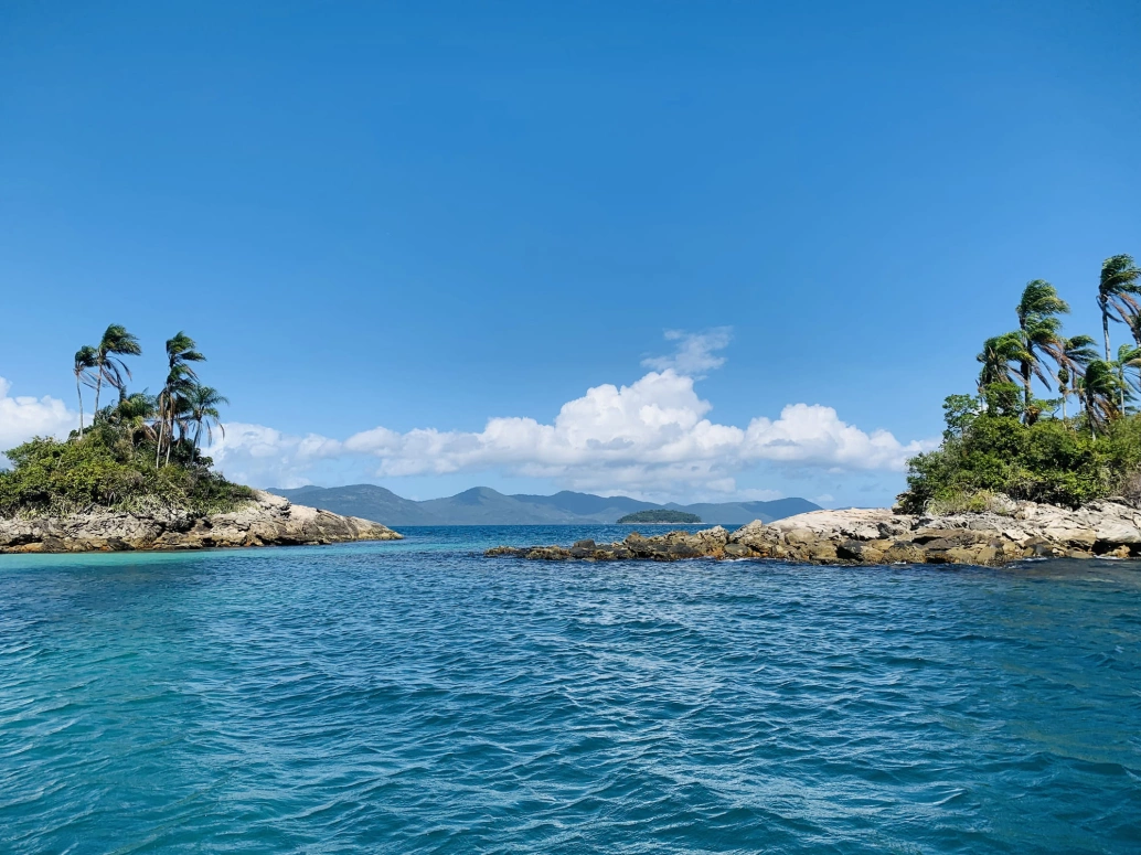 Duas ilhas gêmeas, uma ao lado da outras, cercadas por mar azulado e com coqueiros nos topos de suas pedras