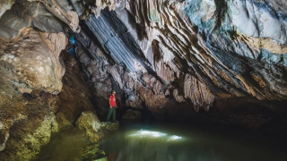 Homem em pé de frente para um poço em meio às estruturas de uma caverna
