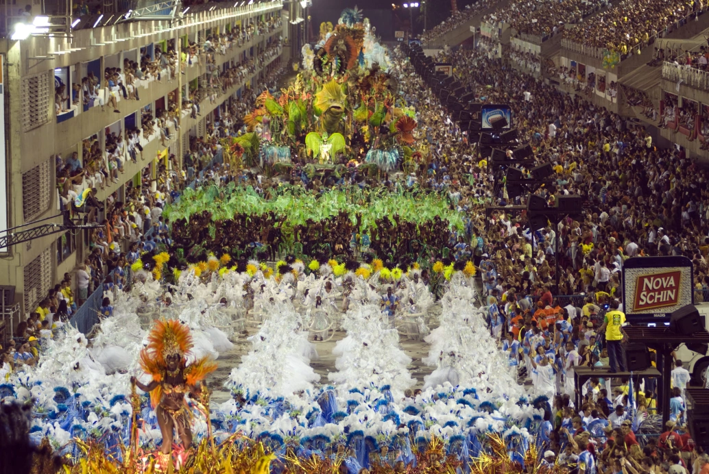 Vista aérea de um desfile de escola de samba no Sambódromo do Rio de Janeiro. As arquibancadas estão cheias de pessoas