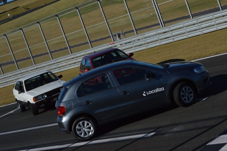 Três versões do carro Gol Volkswagen juntos, em uma pista de corrida. Ao fundo, o gramado e a tela que divide um lado do outro da pista. O dia está ensolarado.