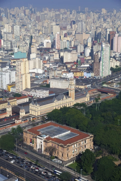 Vista aérea da Pinacoteca de São Paulo, que fica em um prédio em estilo neoclássico. A Estação da Luz aparece logo atrás e, ao fundo, há uma infinidade de edifícios modernos