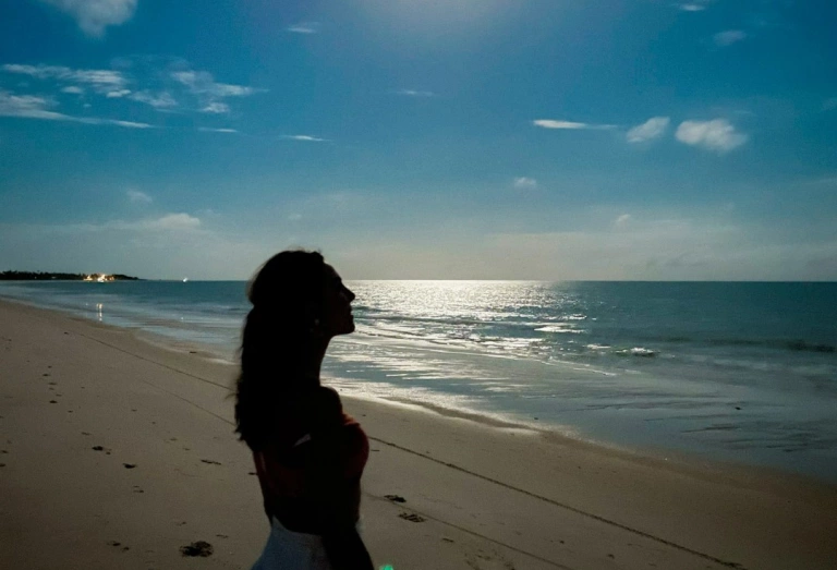 Mulher contempla paisagem de praia deserta olhando em direção ao céu azul