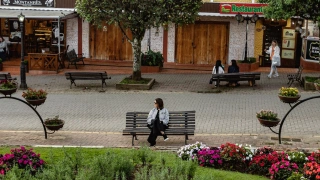 Mulher sentada em banco de praça em meio à cidade pacata.