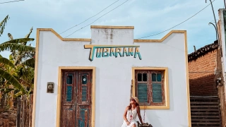 Uma mulher sentada em frente à fachada de uma casa na cor branca