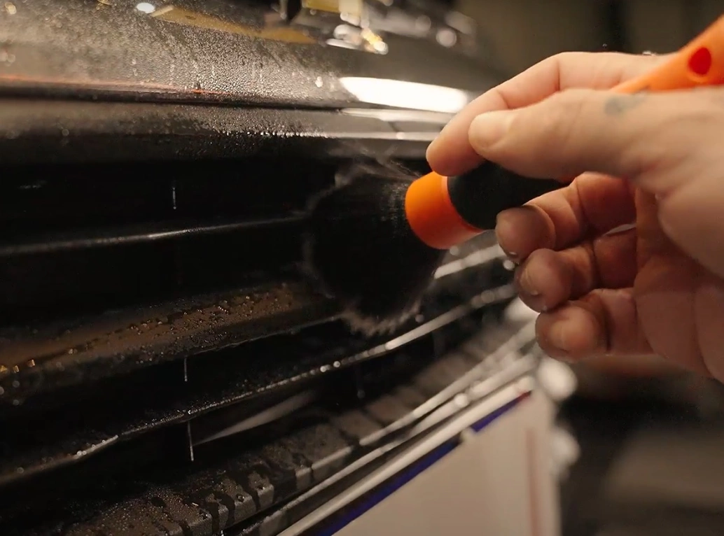 Mão de homem segura pincel repleto de cerdas que limpa gentilmente a superfície de um carro.