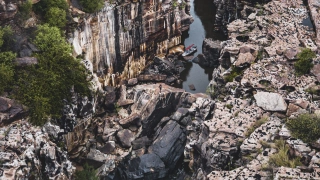 Paredões rochosos nas duas laterais de um rio de coloração escura. A vegetação se espalha ao longo das rochas.