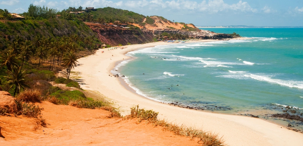 Praia de Pipa (RN). Mar verde-esmeralda, com faixa de areia branca, falésias e vegetação.