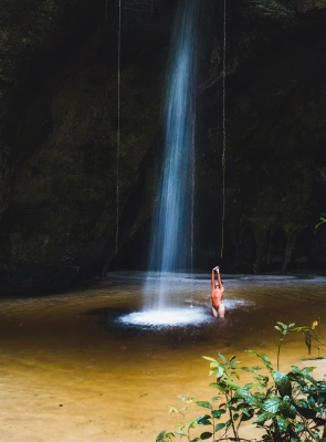 Mulher toma banho de cachoeira dentro de gruta em dia claro