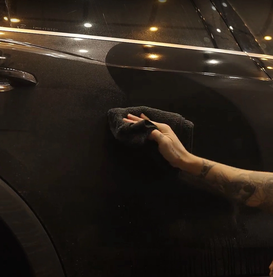 Mão de um homem com tatuagens limpando um carro com pano de microfibra
